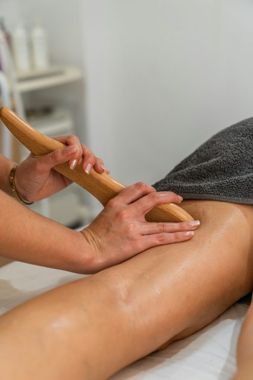Masseuse performing wood therapy treatment on the back of the patient's leg with a wooden board